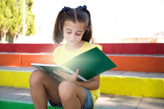 Linda chica sentada en una escalera con los colores de la bandera LGTBI, recogiendo un cuaderno.