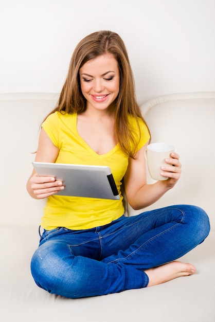 Linda chica sentada con las piernas cruzadas y leyendo noticias en su tablet PC