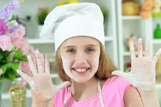 Linda chica con sombrero de chef mostrando las palmas cubiertas de harina