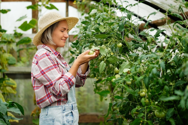 Linda chica con sombrero trabajando en un invernadero. Cosecha de hortalizas de otoño.