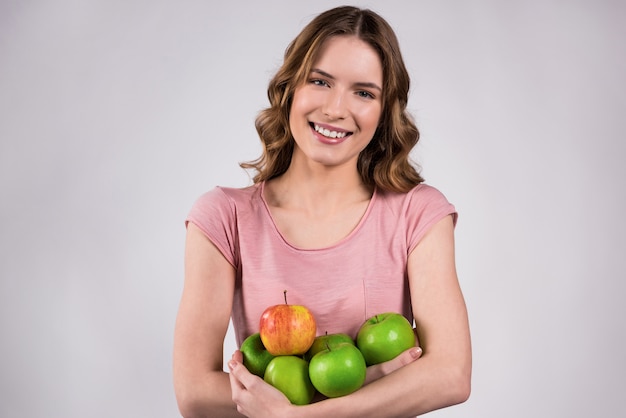 Linda chica sonríe y sostiene deliciosas manzanas en sus manos.