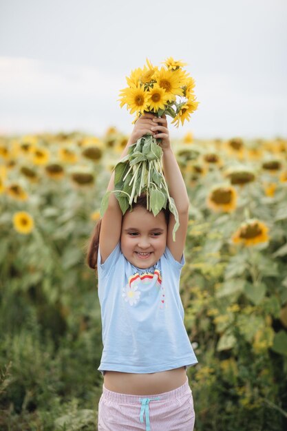 Linda chica sonriente sosteniendo sobre la cabeza un ramo de girasoles en el campo Vacaciones de verano