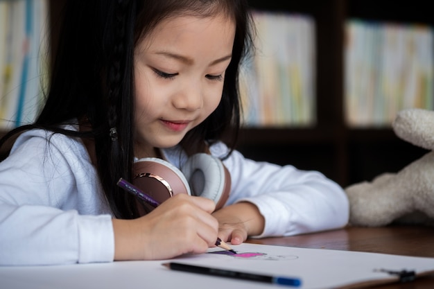 linda chica sonrió y se sienta a dibujar un libro en la biblioteca