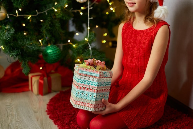 Linda chica sostenga la caja de regalos cerca del árbol de navidad en la mañana en casa