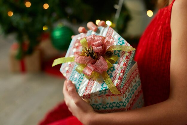 Linda chica sostenga la caja de regalos cerca del árbol de navidad en la mañana en casa