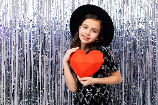 Linda chica sosteniendo un corazón de papel rojo en un brillante