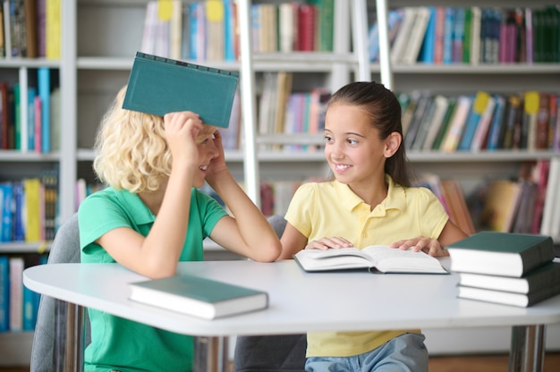 Linda chica y su alegre amiga sentados en una biblioteca