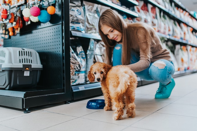 Foto linda chica con su cachorro caniche en la tienda de mascotas.