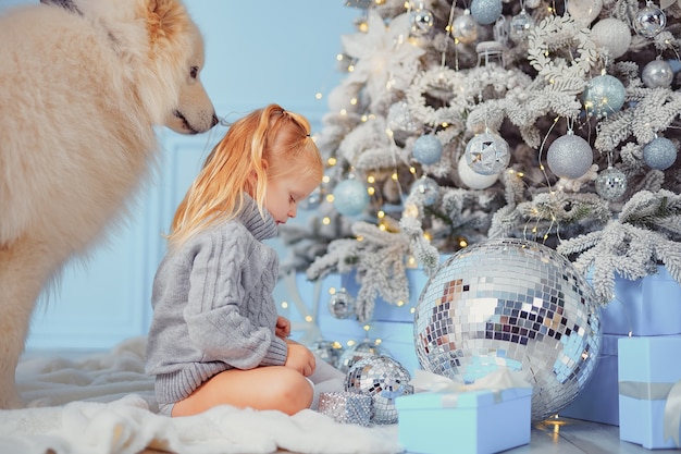 Linda chica con su perro decorando el árbol de Navidad en casa.