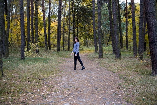 Foto linda chica en un suéter gris es la mitad de una vuelta en el camino en el bosque de otoño.