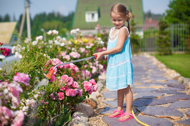 Linda chica en vestido azul regando las flores con una manguera en su jardín