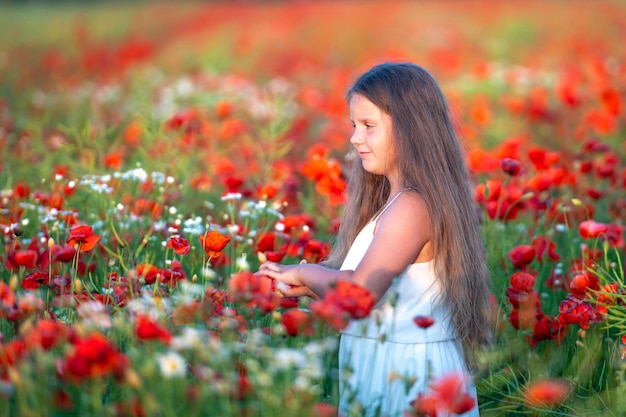 Linda chica con vestido blanco en verano floreciente campo de amapolas caminando bajo el sol de la tarde