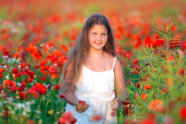 Linda chica con vestido blanco en verano floreciente campo de amapolas caminando bajo el sol de la tarde