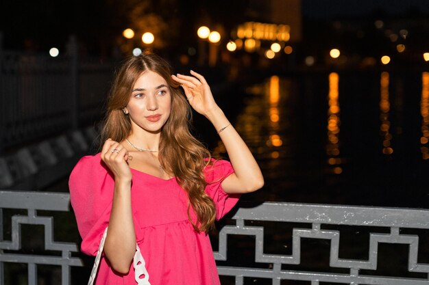 Una linda chica con un vestido elegante camina en un parque cerca de un pequeño lago durante las vacaciones de verano