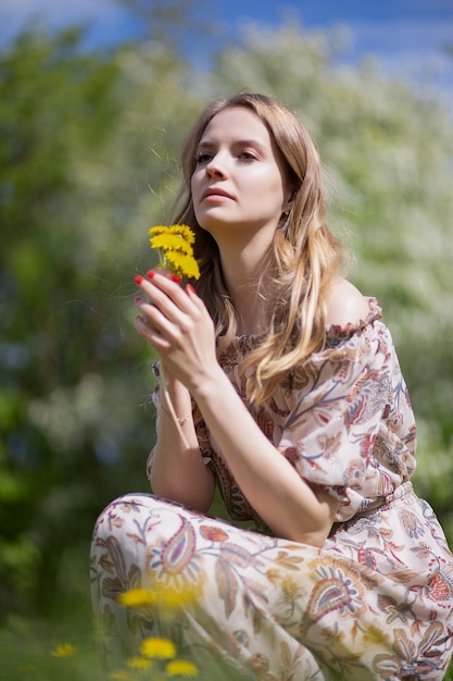 Linda chica en un vestido ligero con un pequeño ramo de flores amarillas