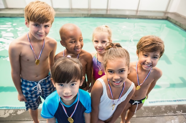 Foto linda clase de natación sonriendo junto a la piscina con medallas