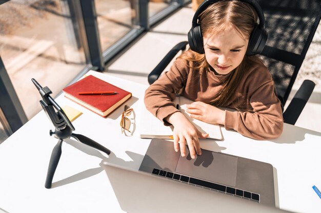 Linda colegial com fones de ouvido trabalhando em um laptop