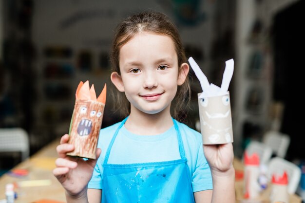 Linda colegial mostrando brinquedos assustadores de halloween feitos à mão feitos de papel enrolado na escola antes do feriado