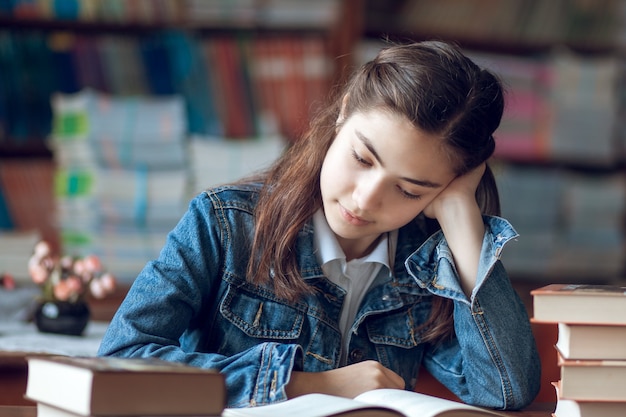 Linda colegial sentada na biblioteca lendo um livro, educação