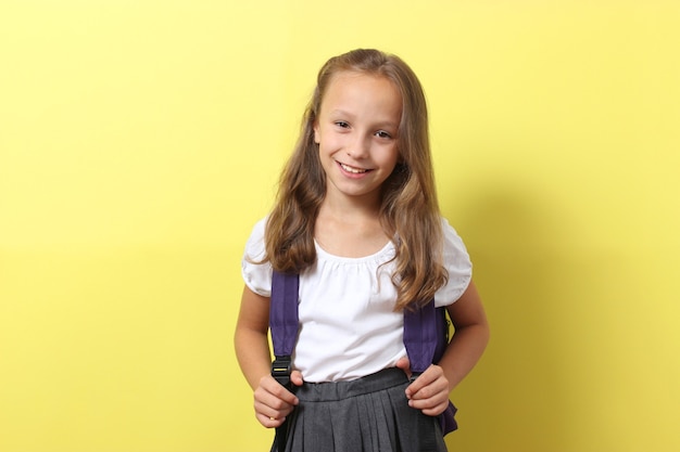 Linda colegial sorridente com uma mochila escolar em um fundo colorido