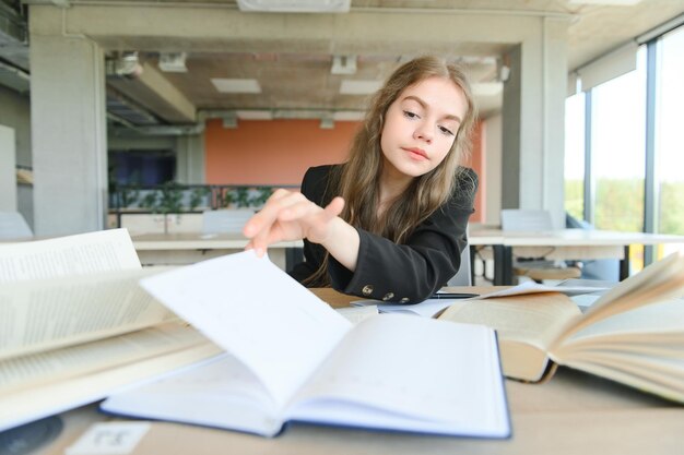 Una linda colegiala de 15 años se sienta en un pupitre escolar con cuadernos, libros y estudios