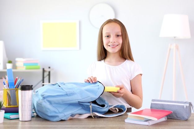 Linda colegiala alegre pone papelería en una mochila