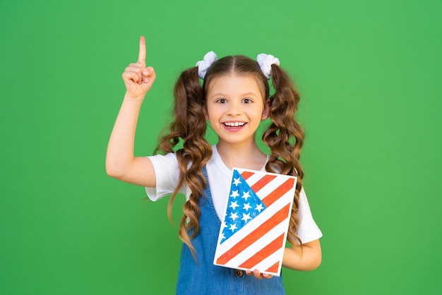 Linda colegiala con un libro de texto y una imagen de la bandera estadounidense Una niña encantadora señala tu anuncio