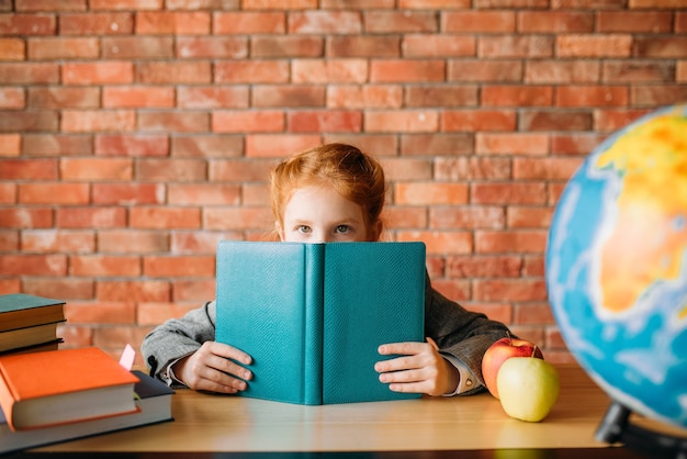 Linda colegiala con libros de texto posa en la mesa.