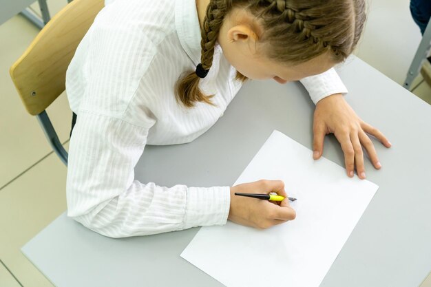 Una linda colegiala sentada en un escritorio de la escuela y escribe en su cuaderno Educación de regreso a la escuela