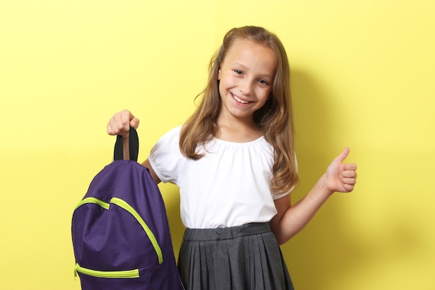 Linda colegiala sonriente con una mochila escolar sobre un fondo de color