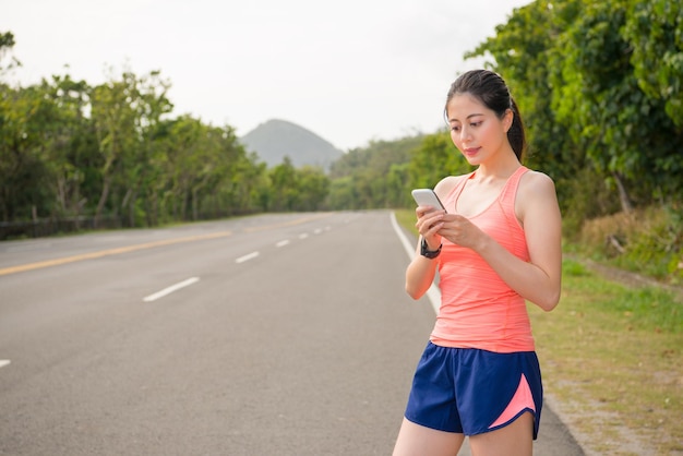 linda corredora de corrida feminina usando smartwatch em pé na rua da estrada usando mensagens de contato de celular celular com amigos após a conclusão do jogo de maratona.