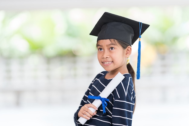 Foto linda criança asiática feliz formada com chapéu de formatura e um diploma isolado no fundo branco