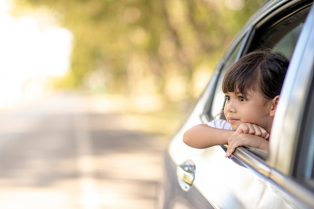 linda criança asiática se divertindo viajando de carro e olhando pela janela