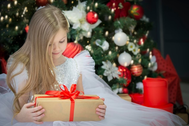 Linda criança com um presente de natal Vestindo a garota na árvore do ano novo