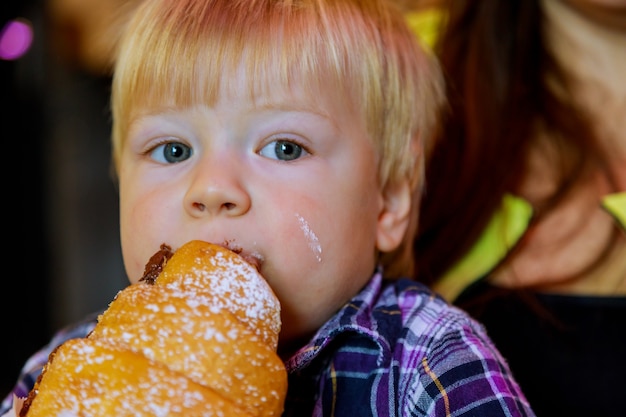 Linda criança comendo pão de croissant de chocolate na mesa em um saco de papel feche a mão garotinho