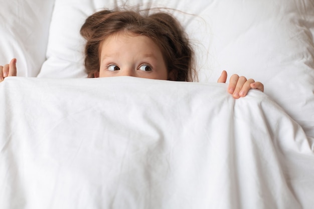 Linda criança menina acordou e deita-se na cama.