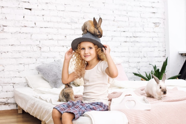 Linda criança menina com cabelo encaracolado e coelhos fofinhos, sentada em um chapéu