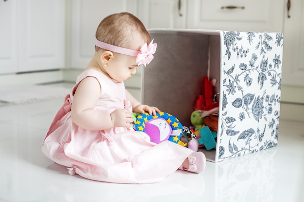 Linda criança recebe brinquedos da caixa. Vestido rosa.