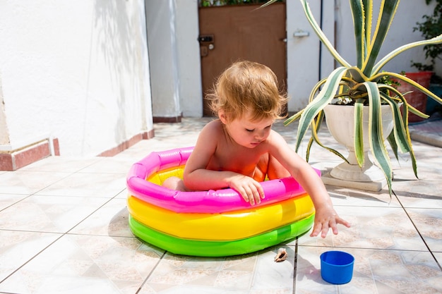 Linda criança se diverte na piscina inflável com brinquedos no verão no quintal