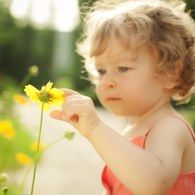 Linda criança tocando a flor amarela da primavera contra o fundo verde natural Foco em primeiro plano