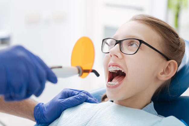 Linda dama adolescente diligente siendo una paciente agradable y sentada quieta mientras recibe el tratamiento necesario de sus dientes