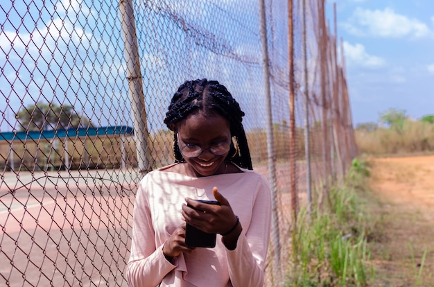 Linda dama africana de pie al aire libre sonríe mientras opera su teléfono celular