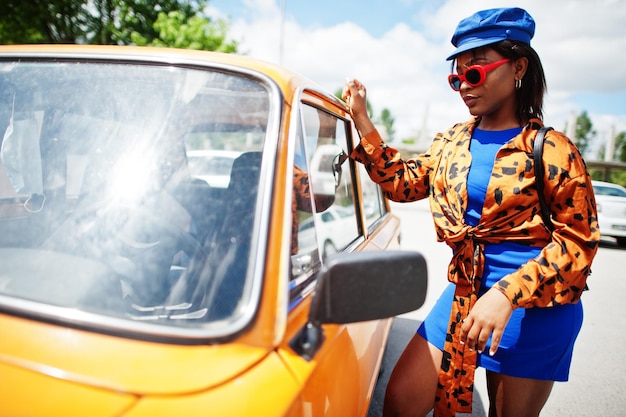 Linda dama afro-americana com óculos de sol em pé perto do carro retrô clássico laranja