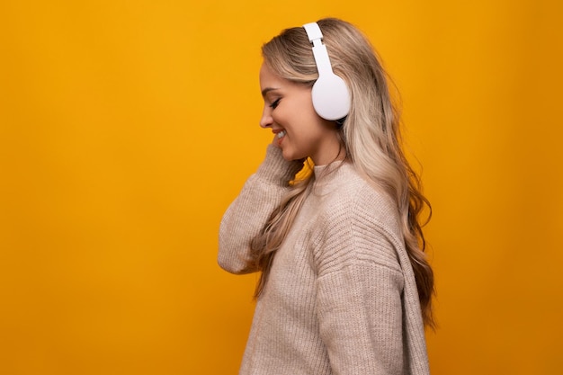 Linda dama escucha alegremente música con grandes auriculares sobre fondo naranja