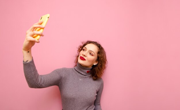 Linda dama con maquillaje y pelo rojo rizado toma selfie en smartphone