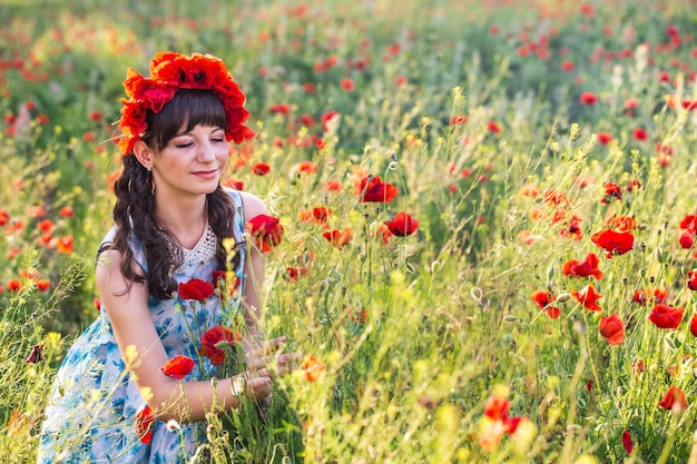 Linda dama romântica no campo de papoulas vestida com vestido casual e guirlanda floral Verão filmado ao pôr do sol