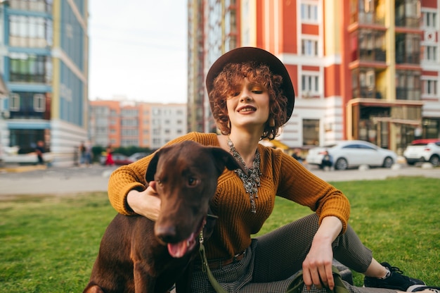 Linda dama con un sombrero relajándose en el césped del patio con una mascota