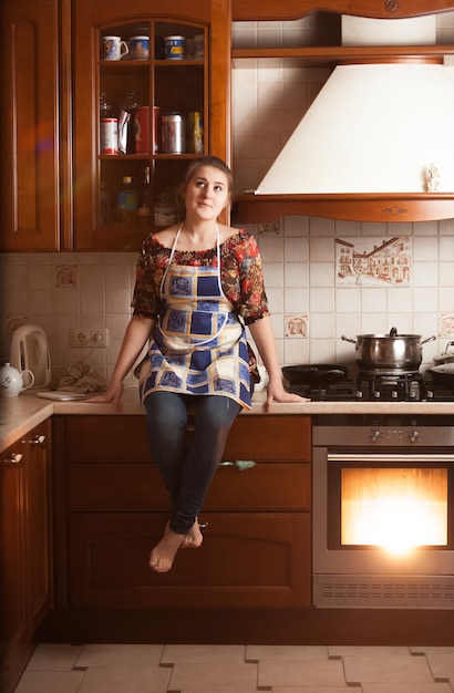 Linda dona de casa sentada na mesa perto de um forno de trabalho