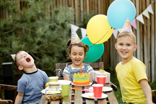 Linda e adorável menina de seis anos comemorando seu aniversário com a família ou amigos com bolo caseiro em uma festa de aniversário de quintal para crianças