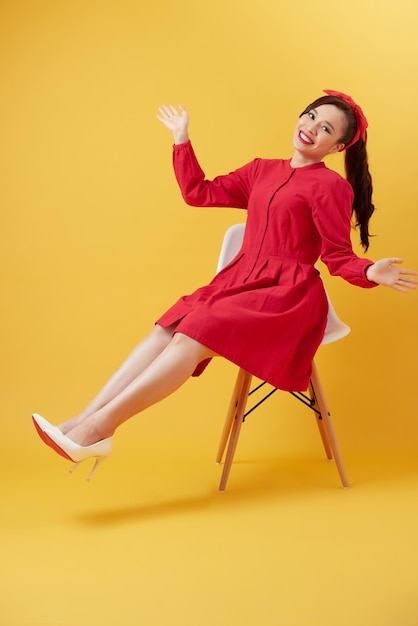 Linda e atraente mulher asiática sentada na cadeira moderna branca e mãos levantadas da felicidade